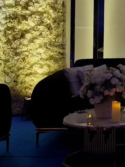 A cozy seating area set against a wall of white roses. The dark sofa and soft candlelight create an intimate and romantic spot for guests at the cocktail party.
