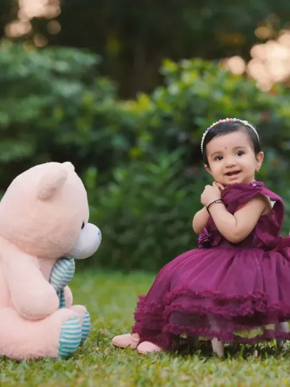 A sweet moment between a little girl and her giant teddy bear during an outdoor park photoshoot. Props like these help create a comfortable and fun environment for children.