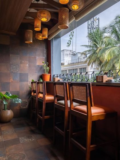 A cozy corner with bar-height seating overlooking the outdoors. The rustic wall tiles and warm wood furniture create a grounded, earthy feel that is both comfortable and stylish.
