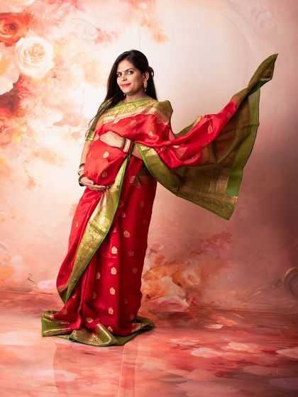 The flowing pallu of the silk saree adds a sense of movement and grace to this elegant studio maternity portrait, set against a beautifully textured backdrop.