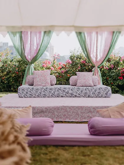 A stunning blend of nature and tradition for an Anand Karaj. This low seating arrangement features pastel pink and green drapes, printed fabrics, and bolsters, creating a soft and elegant atmosphere.