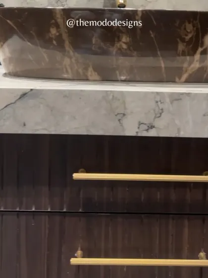 A detail shot of a bathroom vanity, showcasing the beautiful contrast between the dark, fluted wood drawers, the white marble countertop, and the unique brown marble vessel sink.