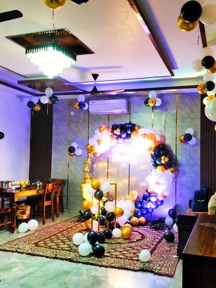 A stylish birthday decoration in a living room. The circular balloon arch in black, white, and gold, along with a neon sign, creates a very modern and chic party corner.