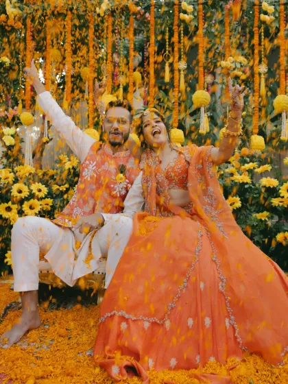 The couple, covered in turmeric and petals, throws their hands up in the air, fully embracing the joyful chaos.