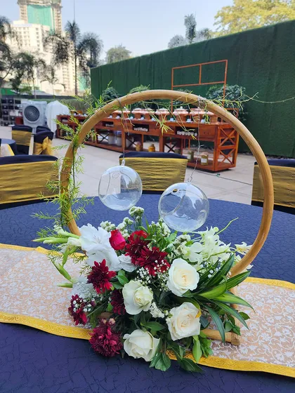 A beautiful circular centerpiece with a mix of red and white flowers. The wooden hoop frame holds two hanging glass baubles, creating a modern and airy design for an outdoor table.