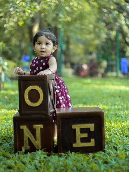 A sweet smile for her first birthday. We captured this moment in a lovely outdoor setting, with the "ONE" blocks marking this special milestone among the green grass.