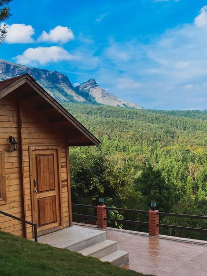 A beautiful wooden cabin in Chikmagalur with the majestic Baba Budan Giri mountain range in the background. The location is perfect for trekkers and nature lovers.