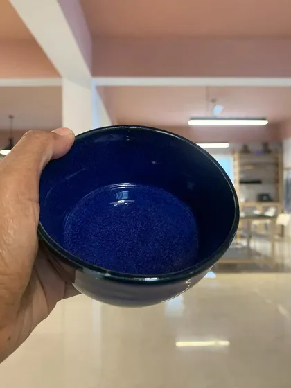 A deep blue glazed bowl held up against the backdrop of our studio. The color is so rich and vibrant after firing.