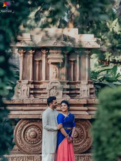 A classic couple portrait in vibrant traditional outfits, perfectly framed by the intricate details of a stone chariot replica.