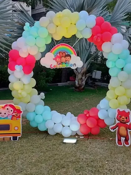An outdoor Cocomelon themed party with a circular rainbow balloon arch. This setup includes character cutouts and is perfect for a garden celebration.
