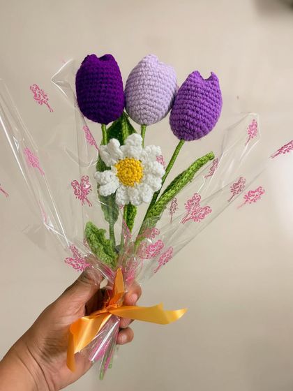 A single tulip and daisy bouquet held in hand. The combination of the purple tulips and the bright white daisy creates a fresh, spring-like feel.
