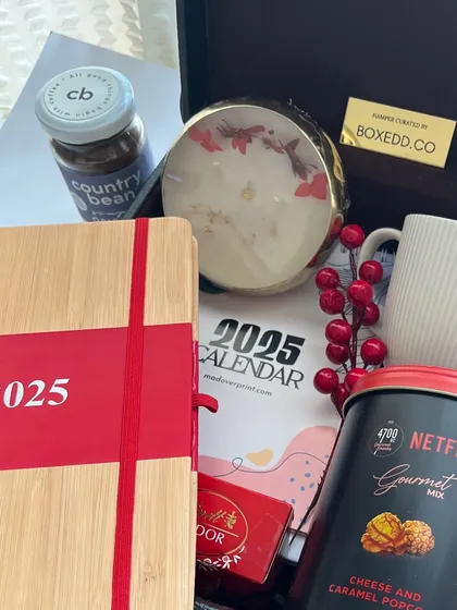 A New Year hamper focused on self-care and productivity. It includes a 2025 calendar, a journal, gourmet popcorn for a "Netflix and chill" vibe, and a scented candle.