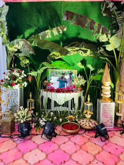 A photo corner with a tropical, South Indian feel, using a backdrop of banana leaves, traditional props, and a framed photo of the couple.