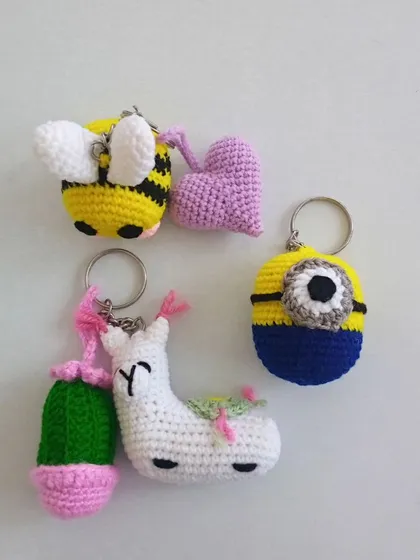 A collection of four of my whimsical crochet keychains. This set includes a bumblebee with a small heart, a character from the movie Minions, and a white llama paired with a tiny cactus, all made with colorful yarn.