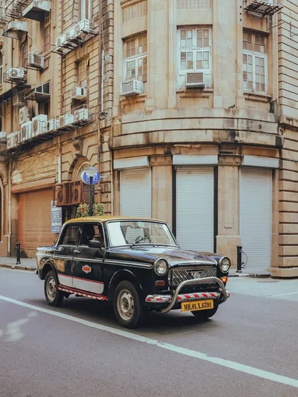 A Premier Padmini taxi turning a corner in the Fort area, with the classic colonial architecture creating a perfect, nostalgic backdrop.