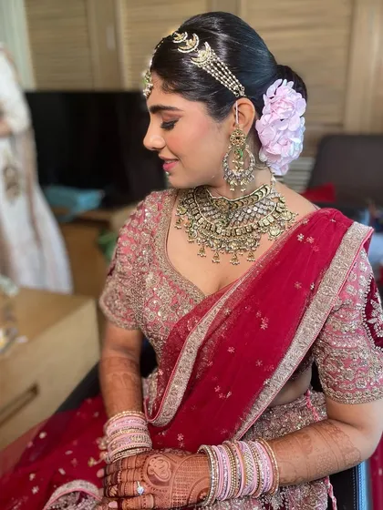 A royal bridal updo featuring a large floral accessory and an ornate matha patti. This is a grand hairstyle for a traditional wedding ceremony.