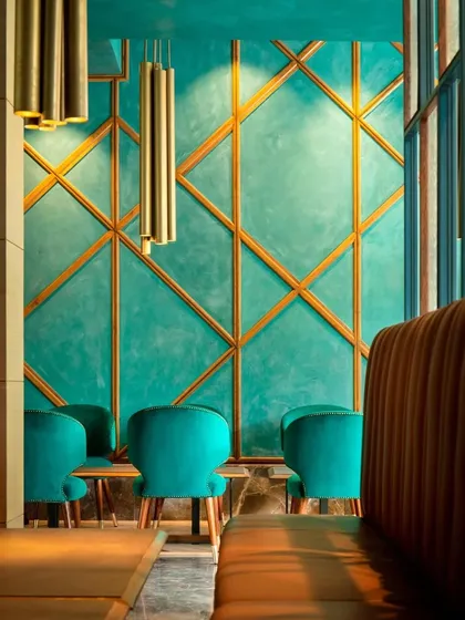 For The Restaurant at Hibiscus, we created a vibrant and immersive dining environment. The design features a bold teal color palette, contrasted with the warmth of leather upholstery and brass accents. The geometric paneling on the wall adds a layer of modern texture, demonstrating our approach to creating unique and memorable commercial and hospitality spaces.