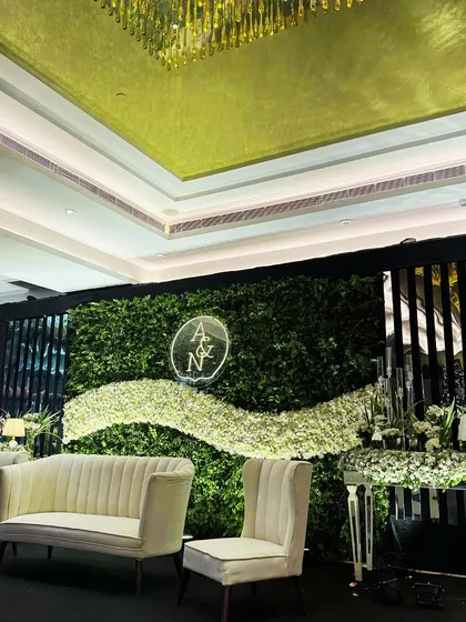 A sophisticated reception stage with a lush green wall, a wave of white flowers, and a custom neon monogram of the couple's initials, combining natural elements with modern chic.
