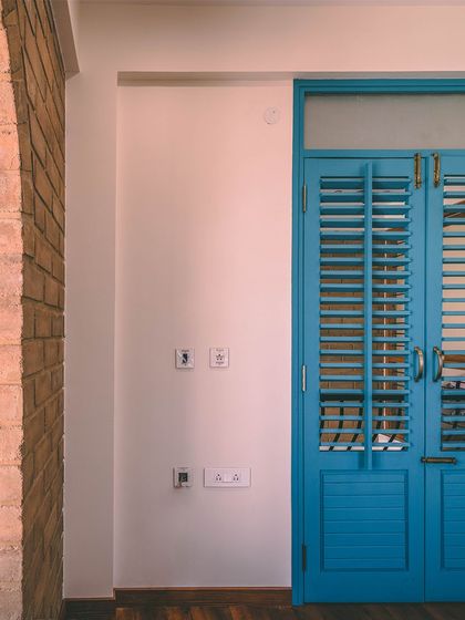 An example of Contrast. The vibrant blue louvered door stands out against the neutral tones of the white wall and the earthy texture of the exposed brick arch, creating visual interest.