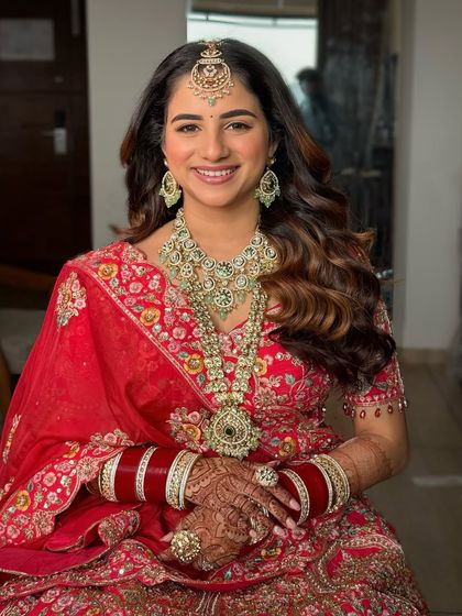A happy, smiling portrait of the bride in her red lehenga. Her soft glam, 'no-makeup' makeup look is a testament to the trend of minimal magnificence.
