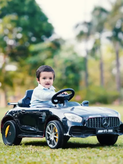 A close-up shot of a toddler enjoying his ride in a miniature car. The focus is on his happy face and the details of this fun prop during an outdoor session.