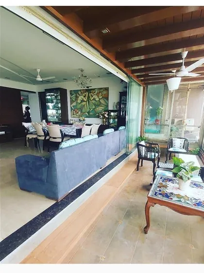 An expansive open-plan living and dining area that opens onto a large, enclosed balcony. The wooden ceiling beams on the balcony add a rustic touch to this modern home.