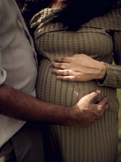 A warm, sunlit close-up of the couple's hands on the baby bump. The light and shadow create a beautiful texture, highlighting their gentle touch.