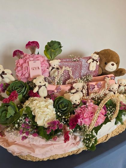 A full view of the pink bassinet hamper, overflowing with gifts, flowers, and teddy bears.