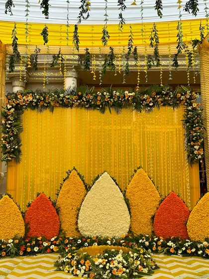 Another angle of the traditional Haldi backdrop, highlighting the hanging green foliage and the beautiful floral border at the top.