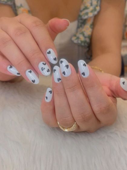 A cute and simple design with a milky white base and tiny black hearts scattered across the nails.