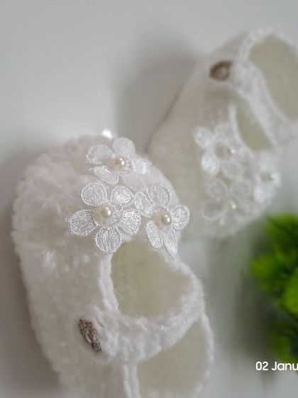 An angled view of the white lace flower booties, showing the secure strap and button closure that keeps them comfortably on your baby's feet.