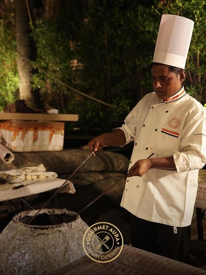 Our chef tends to skewers of kebabs in a traditional tandoor oven at an outdoor event. This authentic cooking method imparts a unique smoky flavor that cannot be replicated.