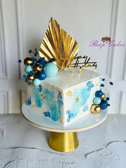 Elegant tropical vibes. This stunning square birthday cake features luxe gold accents, delicate blue stenciling, and a modern touch of edible art.