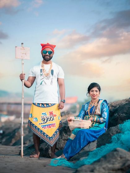 This photo captures the authentic feel of the Agri-Koli lifestyle. The groom holds a sign while the bride sits with a basket, creating a scene that is both a beautiful portrait and a nod to their heritage.