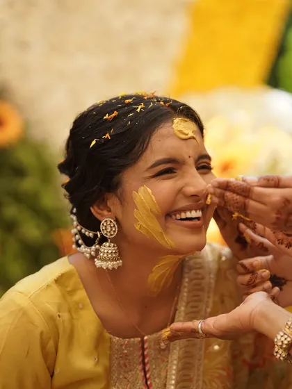 A candid shot from a Haldi ceremony. Even with turmeric on her face, her radiant smile and the hint of her pre-makeup glow shine through. This is pure happiness.