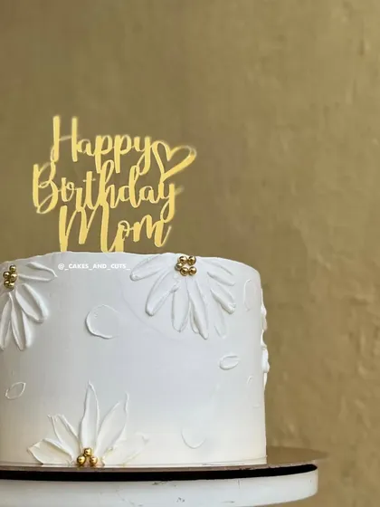A beautiful and simple cake for Mom, decorated with hand-piped daisies and a golden "Happy Birthday Mom" topper.