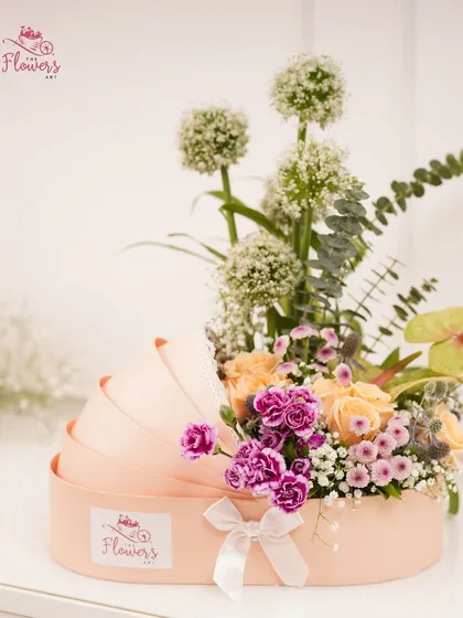 The 'Wild Grace' arrangement is one of my most unique designs, presented in a custom cradle-shaped box. It features striking alliums, soft peach roses, and purple carnations for a truly elegant and memorable floral gift.