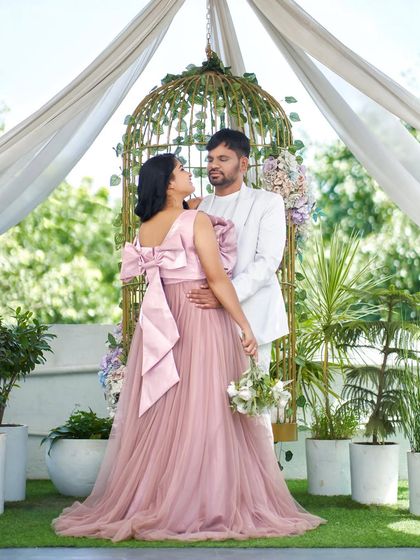 A beautiful maternity shot showing the back of our 'Bloom' gown with its statement bow. The couple is framed by the romantic birdcage setup at our studio.
