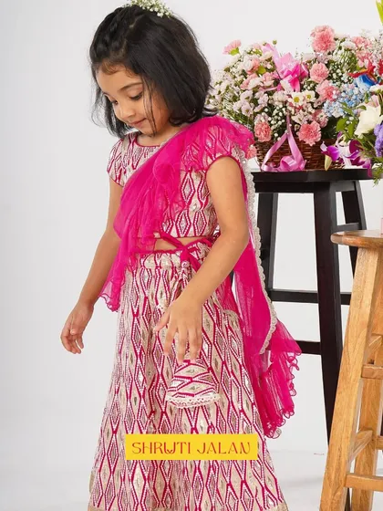 A perfect party dress. This little girl is wearing my pink printed lehenga with a ruffled dupatta, holding a matching little potli bag.