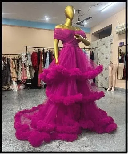 This off-the-shoulder magenta pink ruffled gown is a true statement piece. The layers of tulle create incredible volume and texture for a high-fashion photoshoot look.