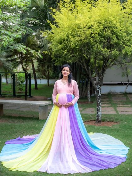 A beautiful full-length portrait of a mom-to-be in our rainbow gown, set against the lovely greenery of a park.