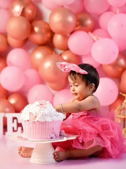 The first touch! Her curiosity takes over as she reaches for the giant pink cupcake, marking the beginning of a fun and memorable cake smash session.
