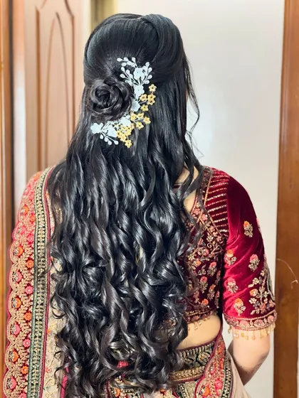 A modern reception hairstyle with a half-updo leading into long, flowing curls, decorated with a delicate floral hairpiece.