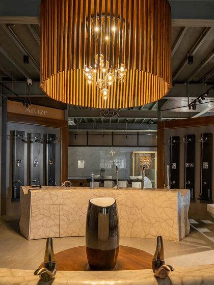 The interior of the Satyam Four Wings showroom, featuring a dramatic central lighting fixture and a marble-clad counter. The design continues the industrial language of the exterior.