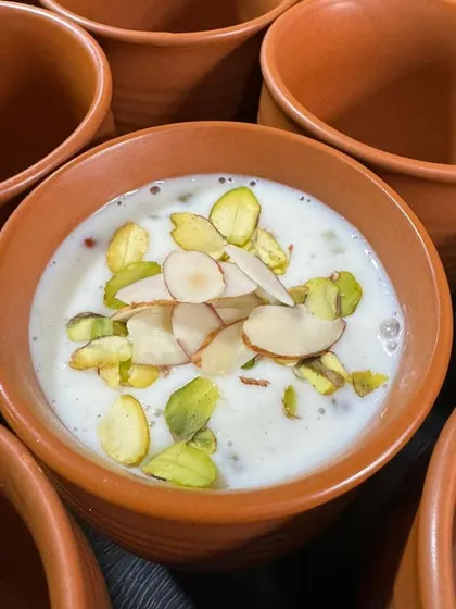 A close-up of our creamy Phirni, a traditional rice pudding, served in an earthy terracotta bowl and garnished with pistachios and almonds.