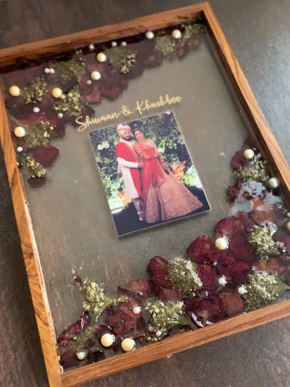 A premium varmala preservation piece in a deep wooden shadow box frame. This design includes the couple's photo and names, surrounded by their preserved wedding flowers.