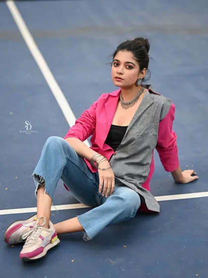A model sits on a tennis court in a chic, color-blocked jacket and jeans. This shot blends sportswear aesthetics with casual fashion for a fresh and modern editorial look.