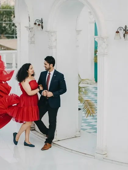 A dynamic and playful shot of the couple, with the bride's vibrant red dress caught in motion. This image is full of energy and style, set against a clean, white architectural backdrop.