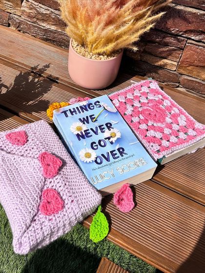 A flat-lay of two different book cover designs: a purple one with hearts and a pink granny square version.