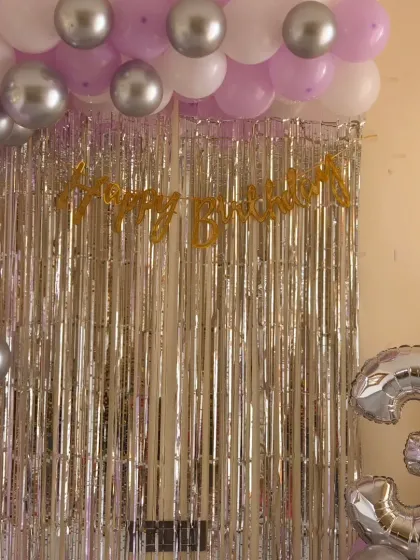 An elegant home setup for a 3rd birthday using a silver shimmer curtain with lavender and silver balloons. It's a simple way to make a milestone feel special without a big budget.
